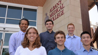 5 aspiring Albany Medical College students stand on the steps of the college entrance with Dr. Arup De as part of the inaugural Albany Med Health Corps team