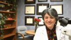 Nada Farhat, MD, ocular pathologist, sits at her desk in front of a microscope.