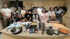 A group of children, parents, and doctors in a kitchen, posing around the stove after cooking a meal together.