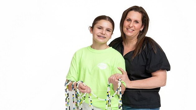 Mom and daughter pose for a picture. The daughter is holding a long strand of beads. They are her "beads of courage"
