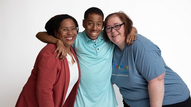 A boy, his mom, and his nurse pose for a picture. The boy is in the middle with his arms around their necks