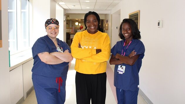 Three women in scrubs standing in a hospital hallway