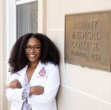 Medical student leans up against a building next to an Albany Medical College sign