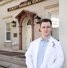 Medical student leans up against a building next to an Albany Medical College sign