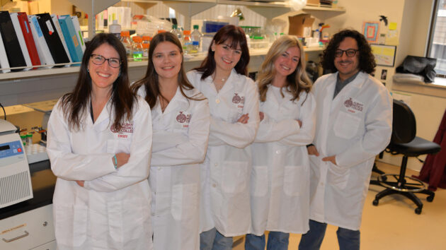 Five scientists wearing white coats standing in a research lab