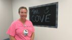 Nurse standing in front of a chalkboard sign that says The Cove