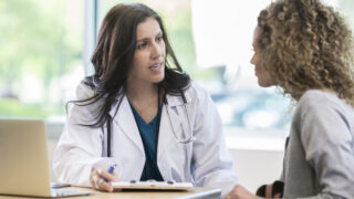 Concerned female doctor discusses a diagnosis with a young female patient. The doctor has a serious expression on her face.