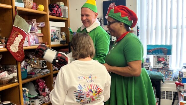 A man and a woman, dressed like elves, helping a girl pick out christmas presents