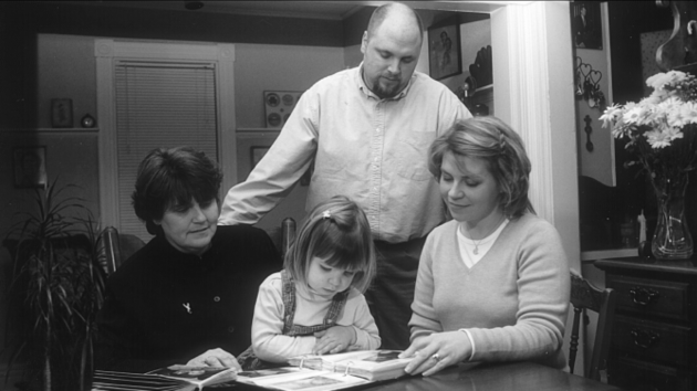 A black and white picture of a family looking at a photo album