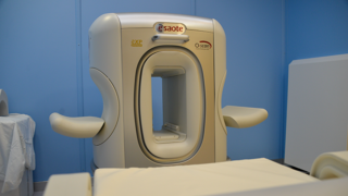 A non-immersive extremity magnetic resonance imaging (MRI) machine sits against a blue wall in a medical office.