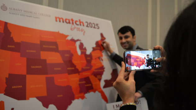 A medical student shows where he matched on a map of the U.S. while someone else takes a photo at Match Day 2025