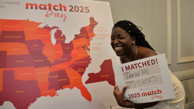 A medical student standing in front of a map of the U.S. holding a sign showing where she matched at Albany Medical College's Match Day 2025